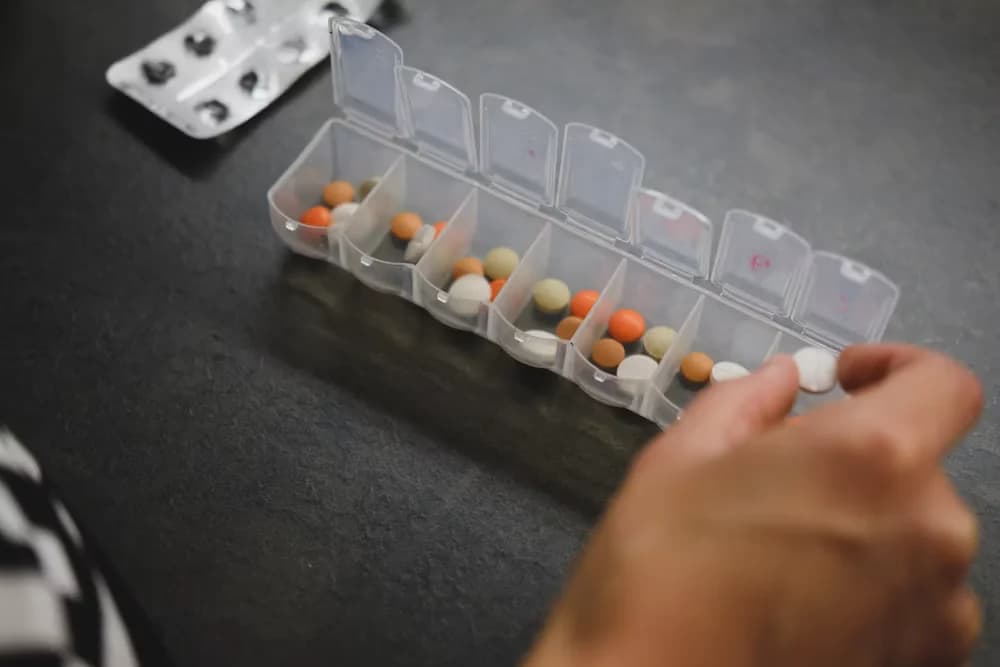 A hand sorting medication from a weekly pill organizer